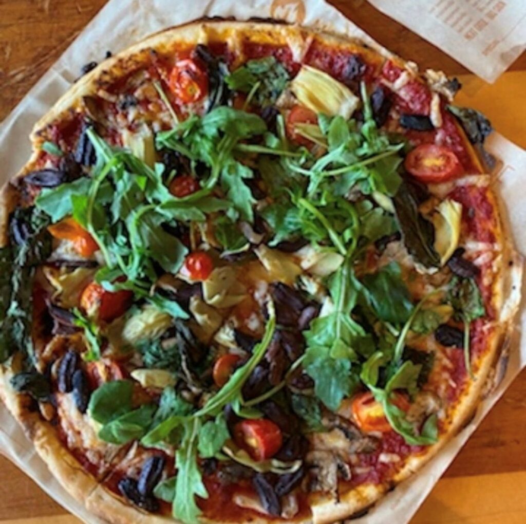 Vegan and Gluten free pizza topped with veggies topped with fresh arugula